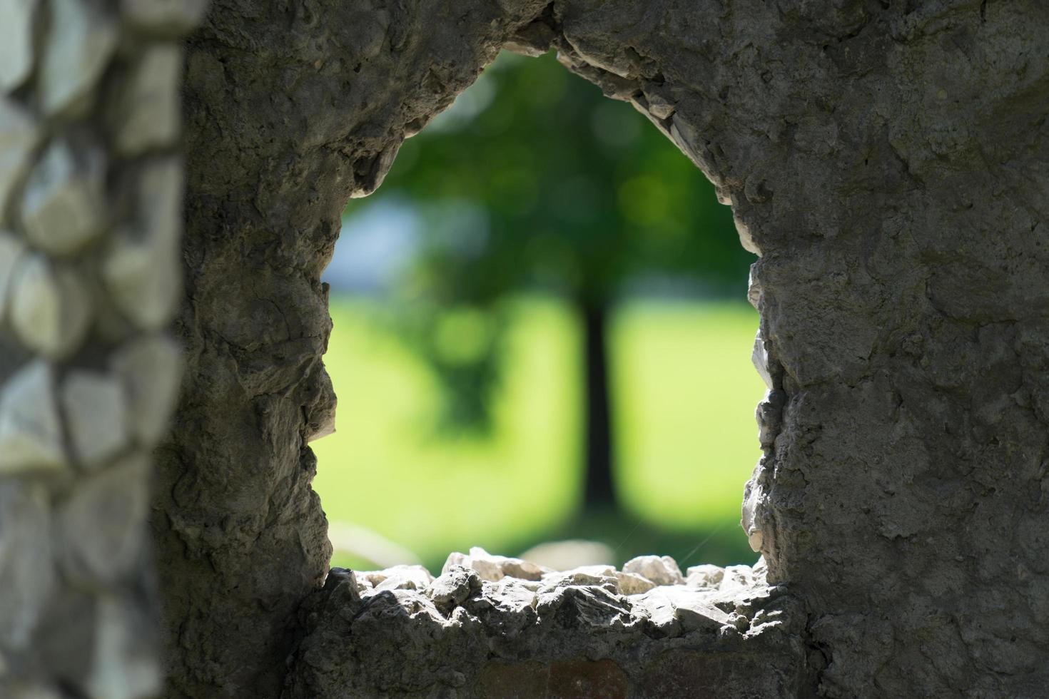 Muro de piedra con ventana recortada con árbol borrosa en el fondo foto