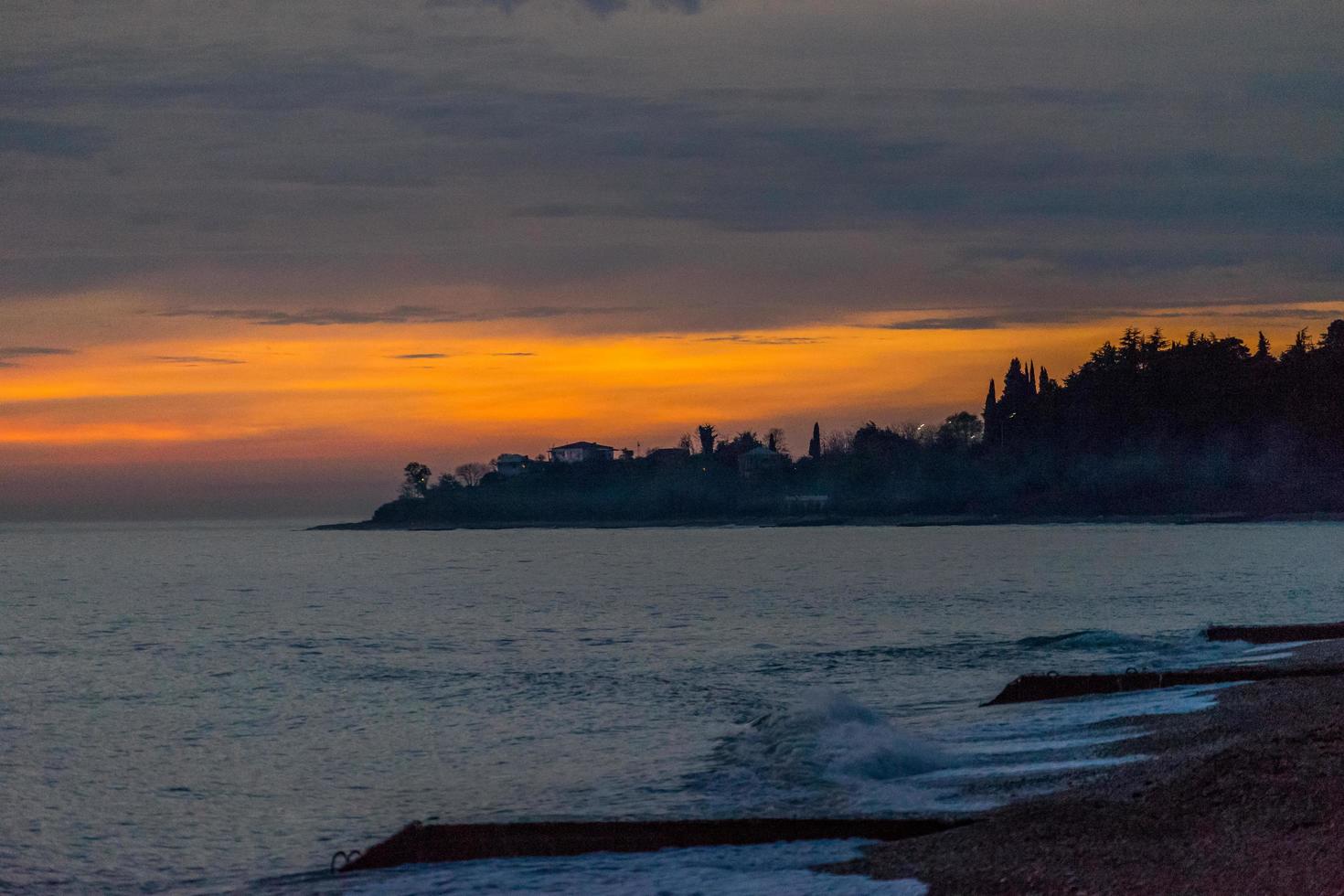 Colorido atardecer rojo sobre un cuerpo de agua junto a una costa en Abjasia foto