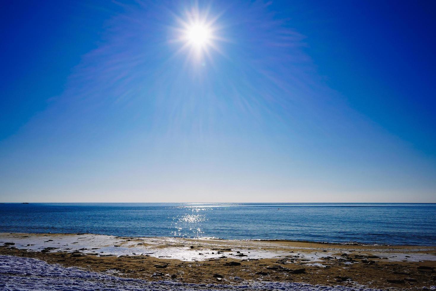 Seascape of a shoreline and a body of water with bright sun and a clear blue sky photo