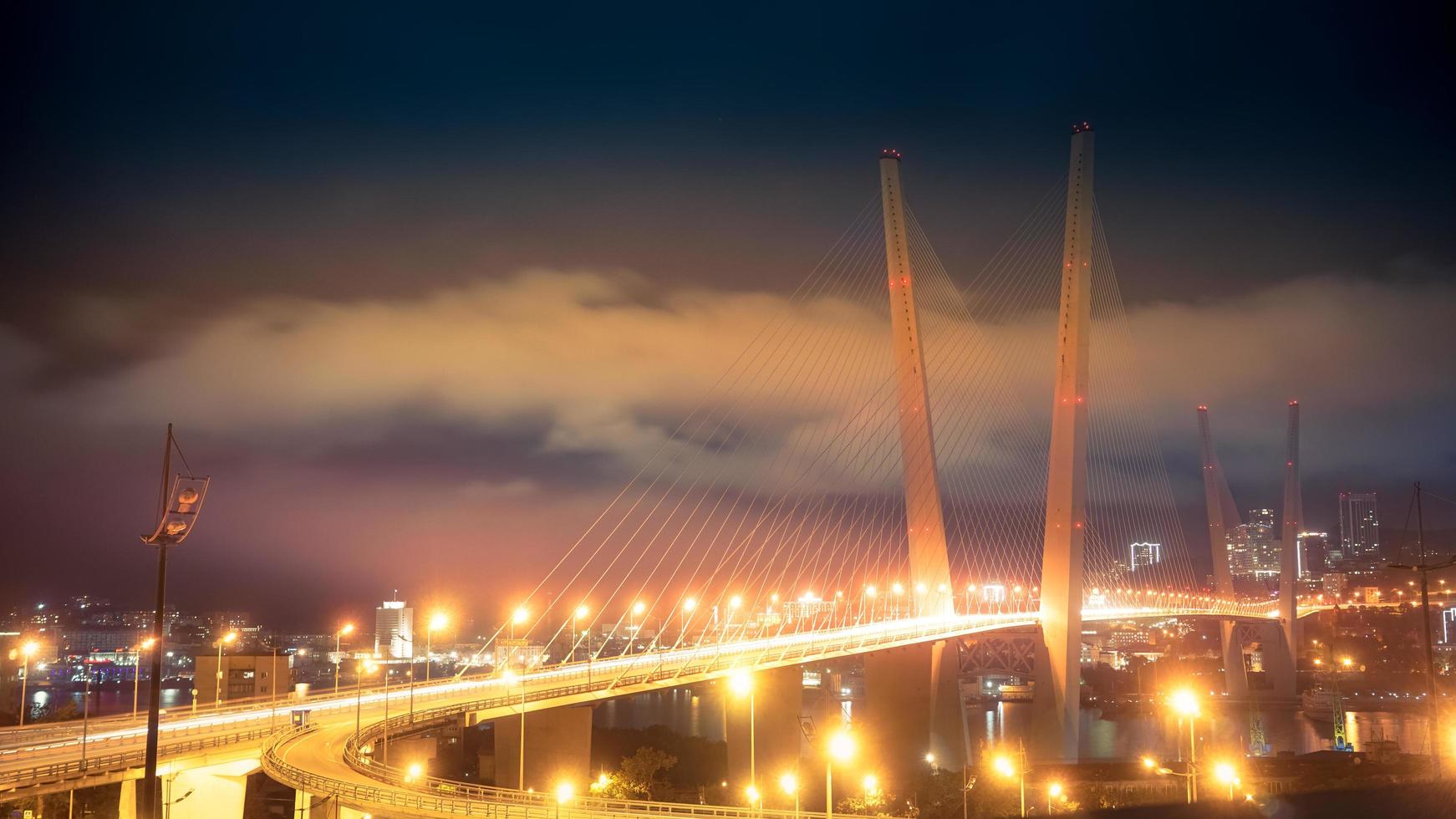 Iluminado puente dorado con cielo nublado por la noche en Vladivostok, Rusia foto