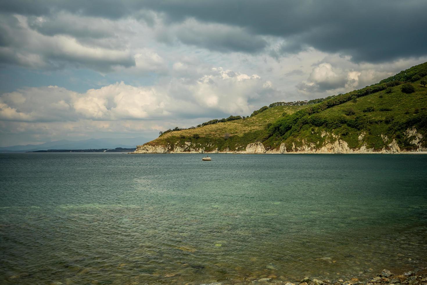 Paisaje marino de una costa rocosa en un cuerpo de agua con montañas y cielo azul nublado en Nakhodka, Rusia foto