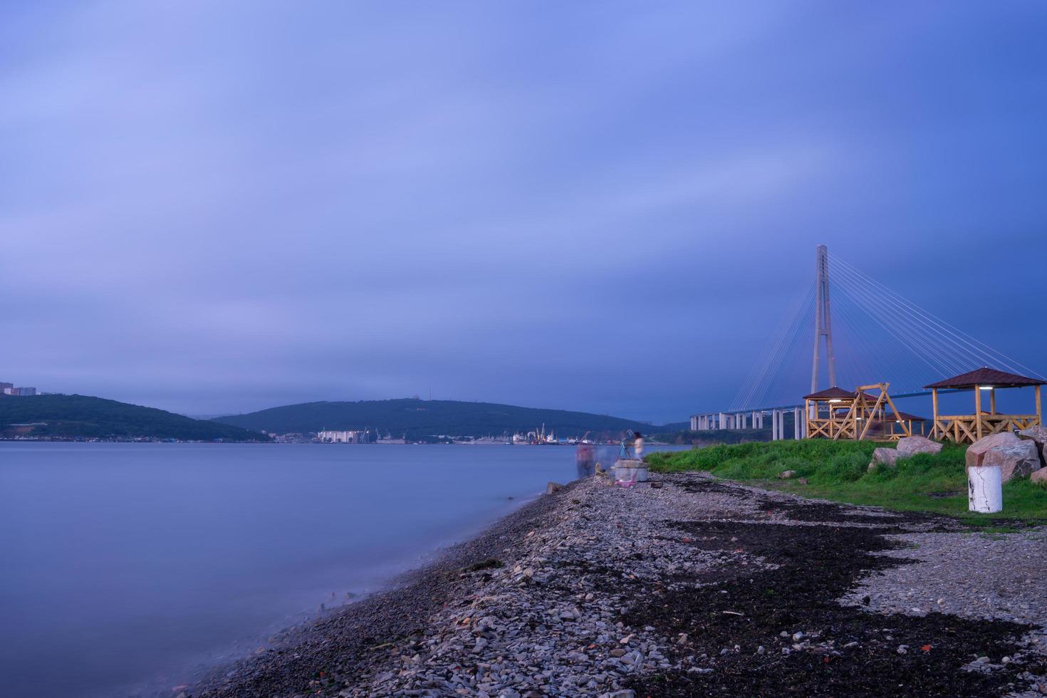 Vista de la costa rocosa con el puente russky en el fondo y un cuerpo de agua en Vladivostok, Rusia foto