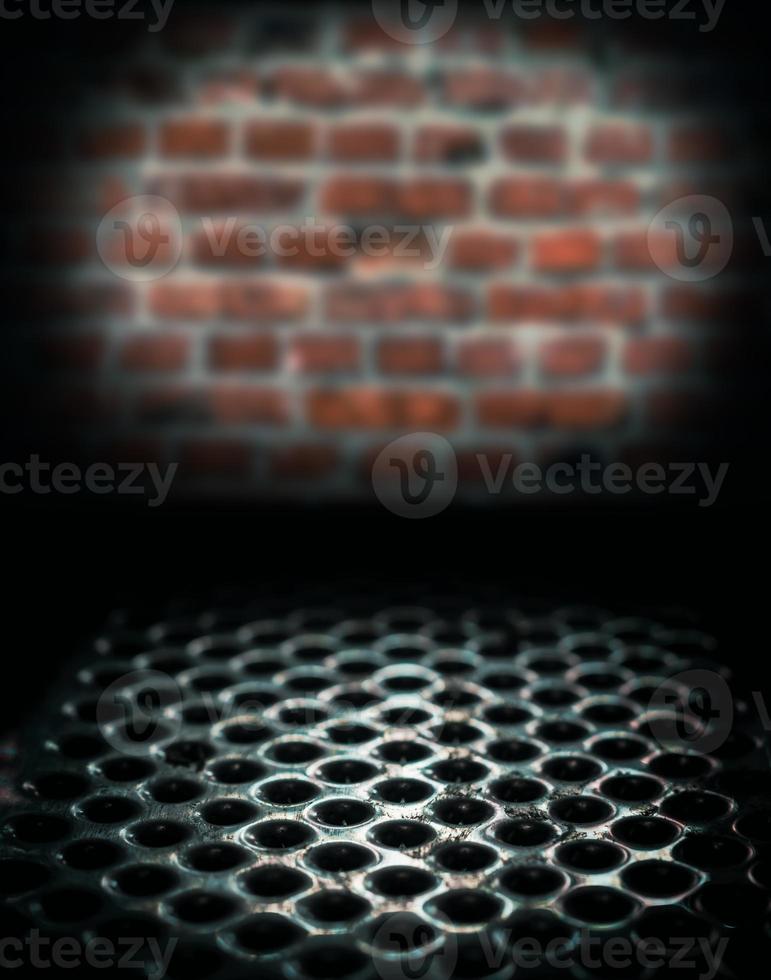 Metal perforated table surface in a dark basement against a brick wall, close up horror background photo