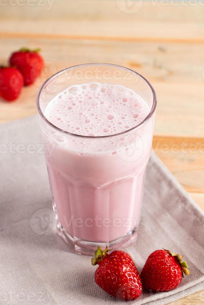 Milkshake with strawberries. Cold summer drink with berries on wooden background. photo