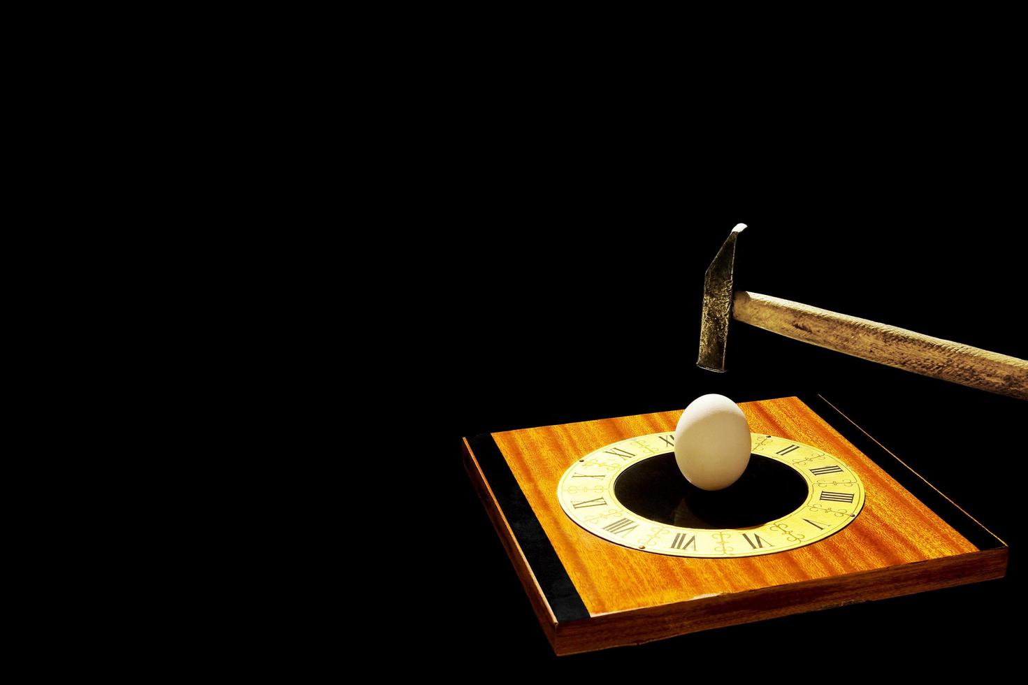 objetos abstractos aislados sobre fondo negro. un martillo rompiendo un huevo en una esfera de reloj vintage. foto
