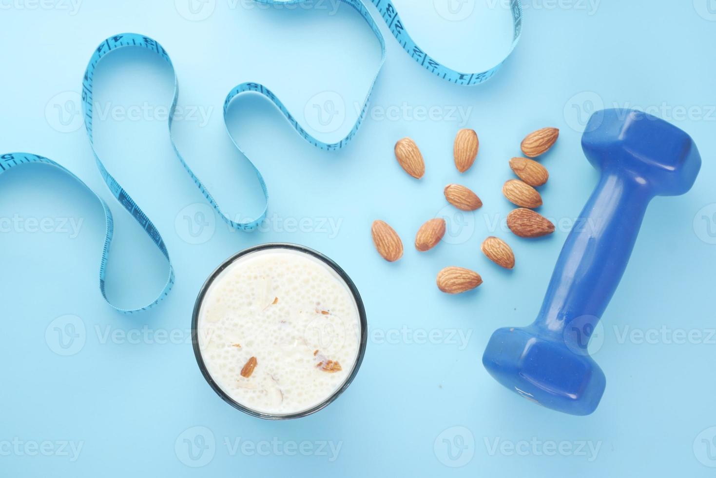 Top view of a measuring tape, dumbbell, almond nuts and milk on blue background photo