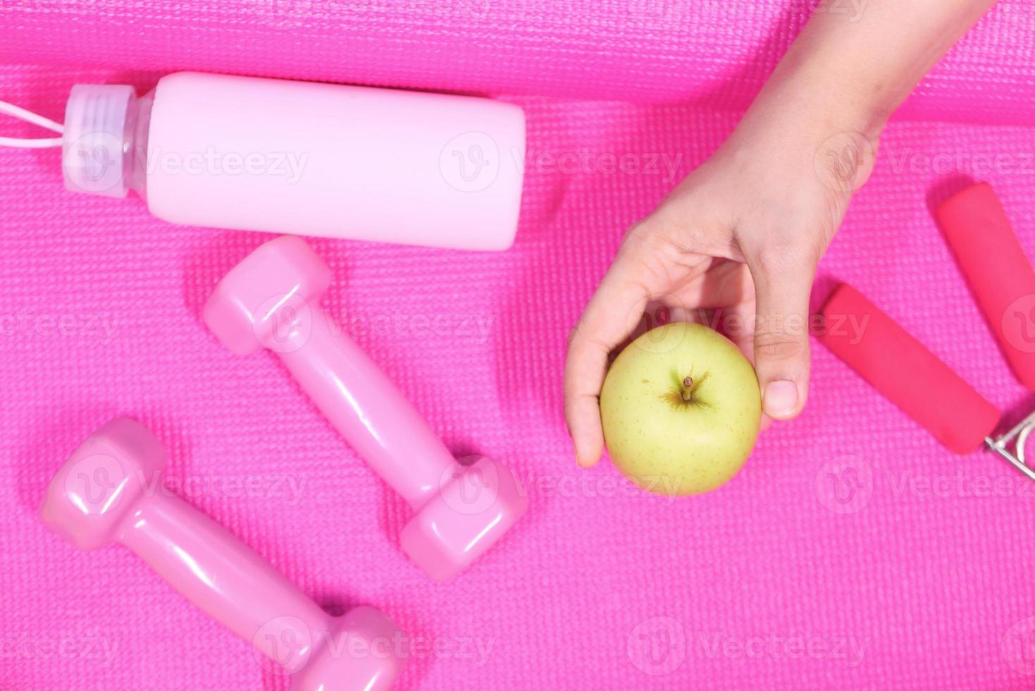 Hand holding an apple with workout equipment photo