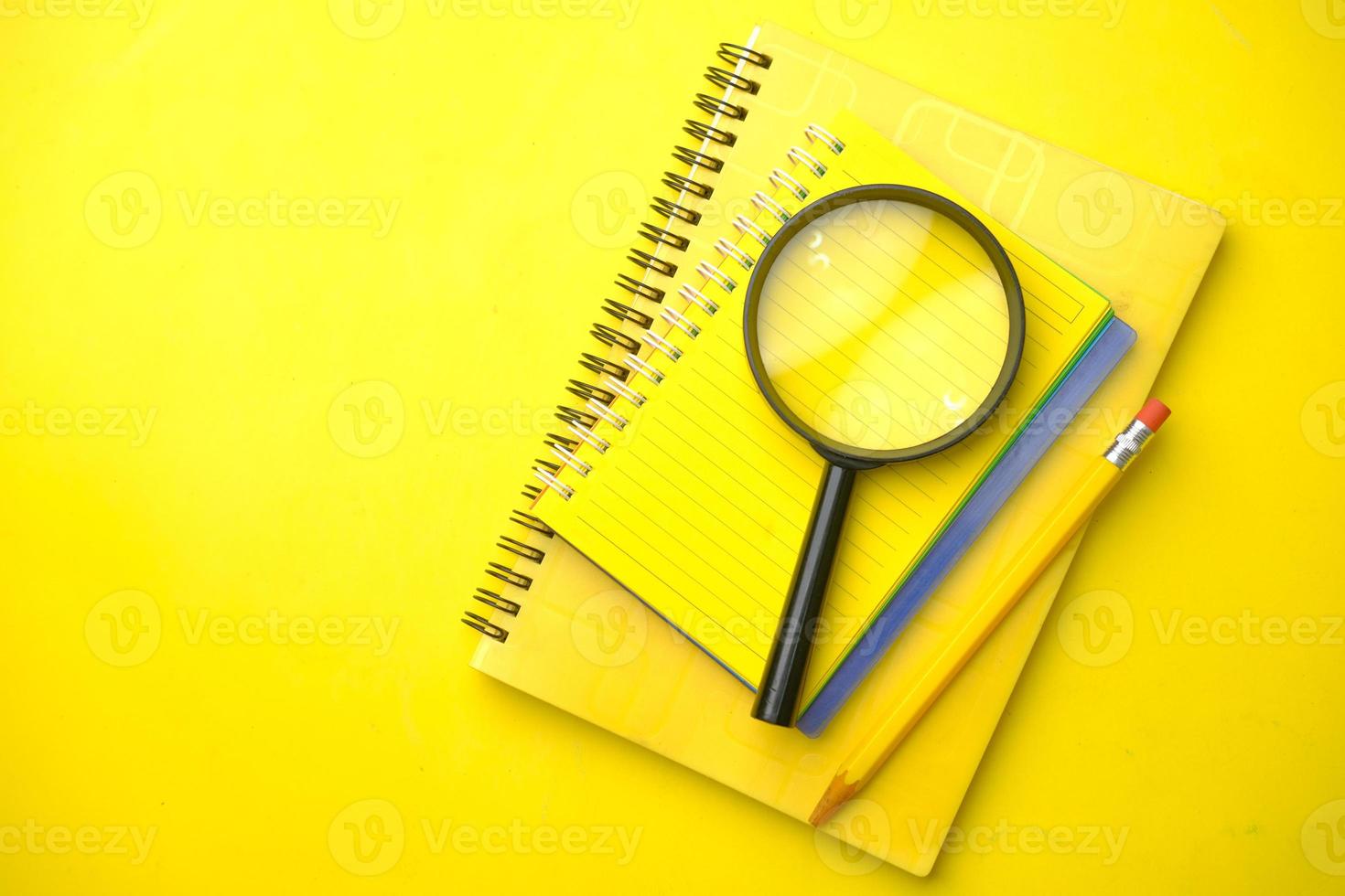 cuaderno amarillo y lápiz con lupa foto