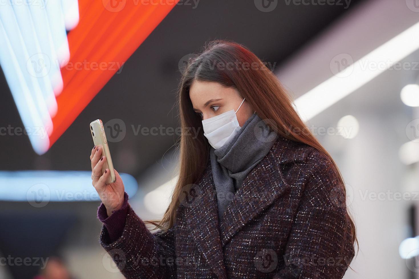 una mujer con una mascarilla médica está esperando un tren y sosteniendo un teléfono inteligente foto