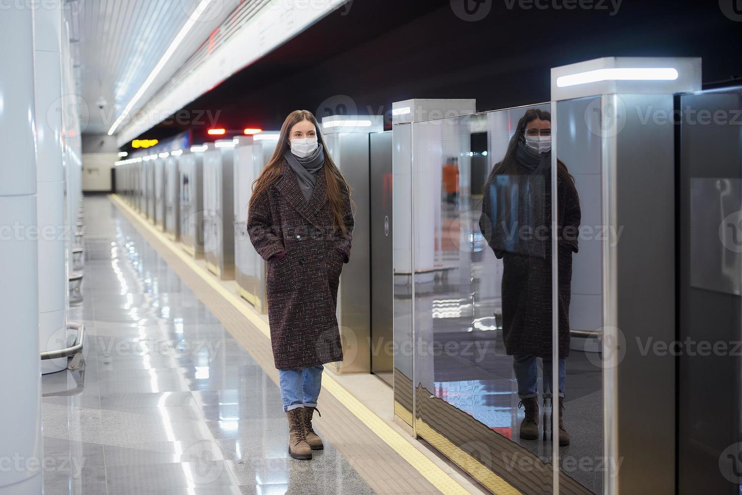 Woman in a medical face mask is standing near the departing train on the subway photo