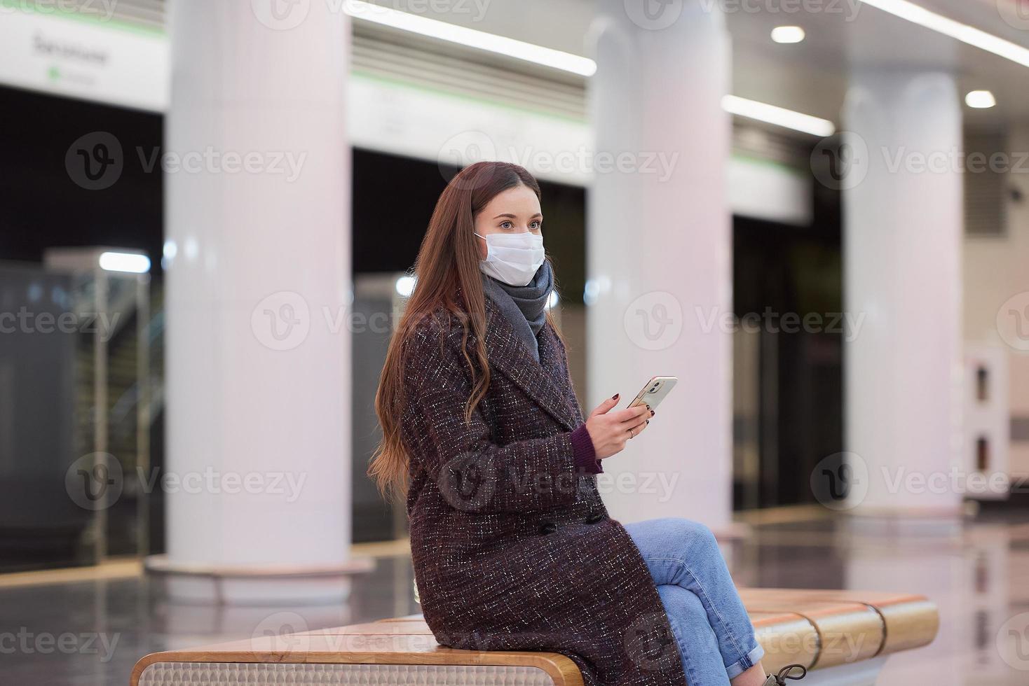 una mujer con una mascarilla médica está esperando un tren y sosteniendo un teléfono inteligente foto