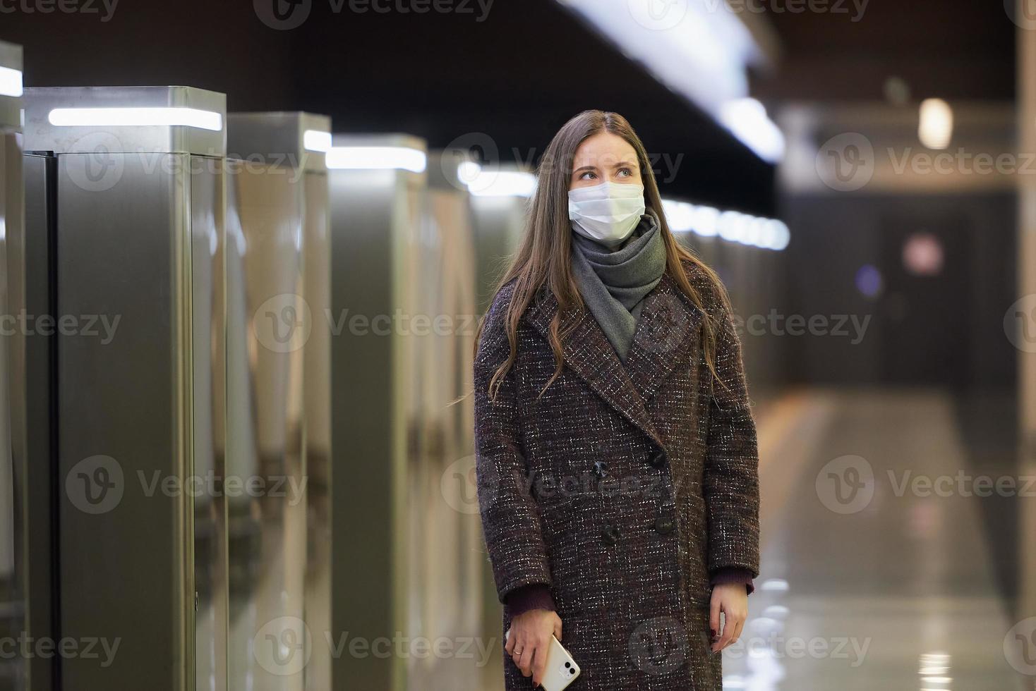 una mujer con una mascarilla médica está esperando un tren y sosteniendo un teléfono inteligente foto