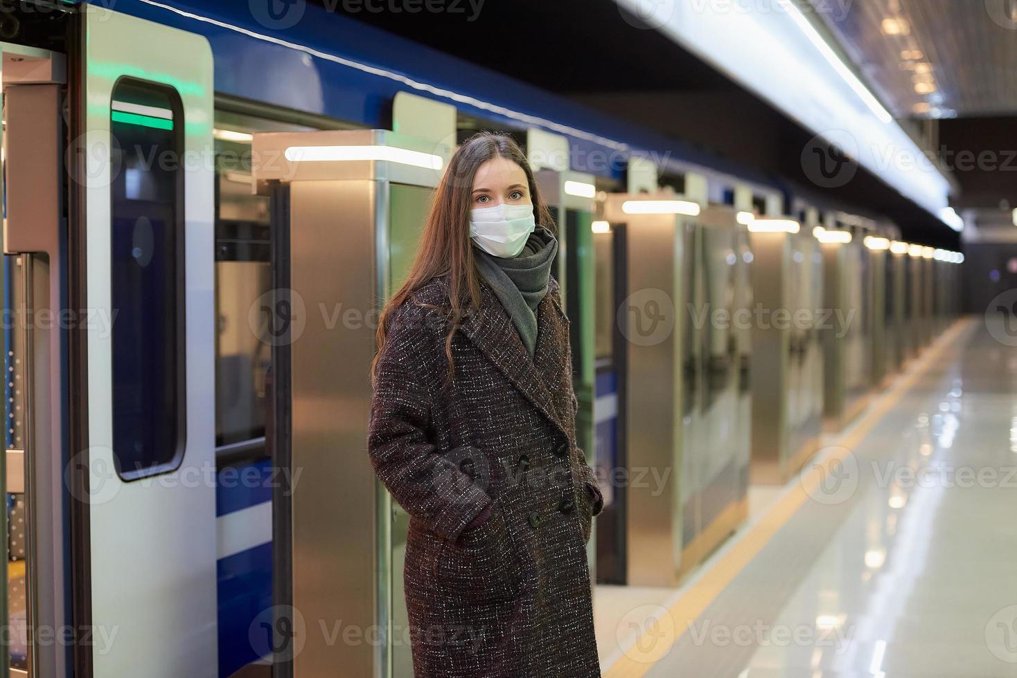 A girl in a surgical face mask is keeping social distance on a subway station photo