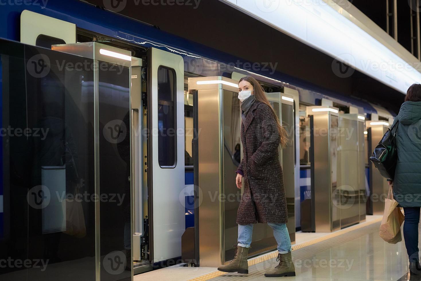 A girl in a surgical face mask is keeping social distance on a subway station photo