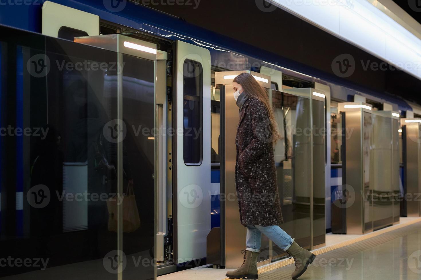 una niña con una mascarilla quirúrgica mantiene la distancia social en una estación de metro foto