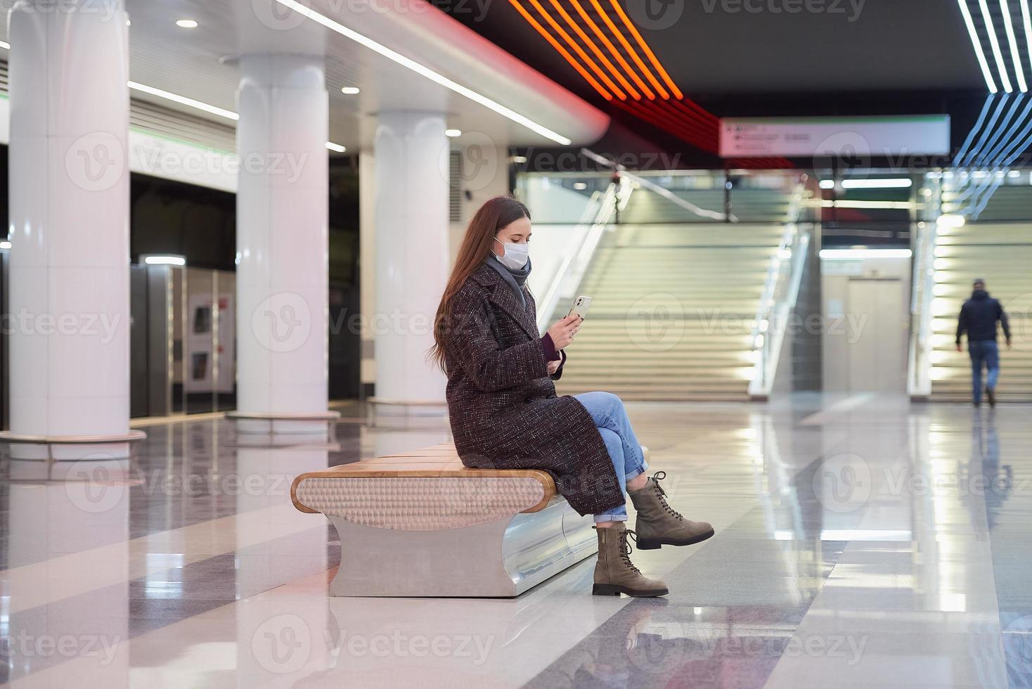 A woman in a medical face mask is waiting for a train and holding a smartphone photo
