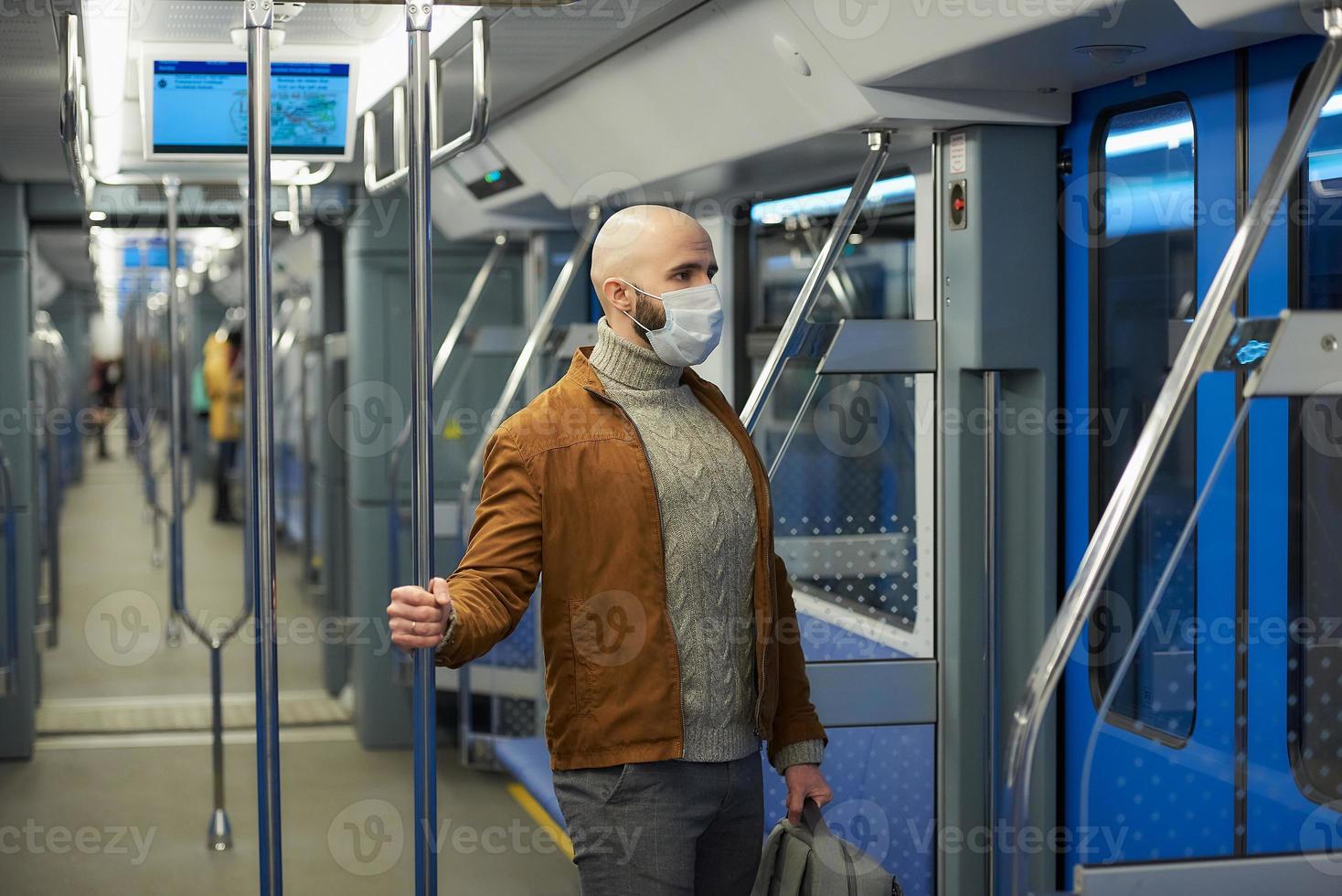 Un hombre calvo con barba en una mascarilla está sosteniendo el pasamanos en un vagón de metro foto