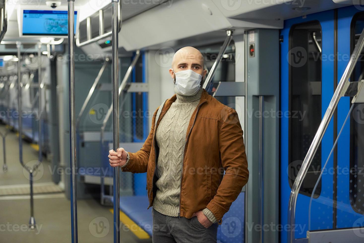 Un hombre calvo con barba en una mascarilla está sosteniendo el pasamanos en un vagón de metro foto