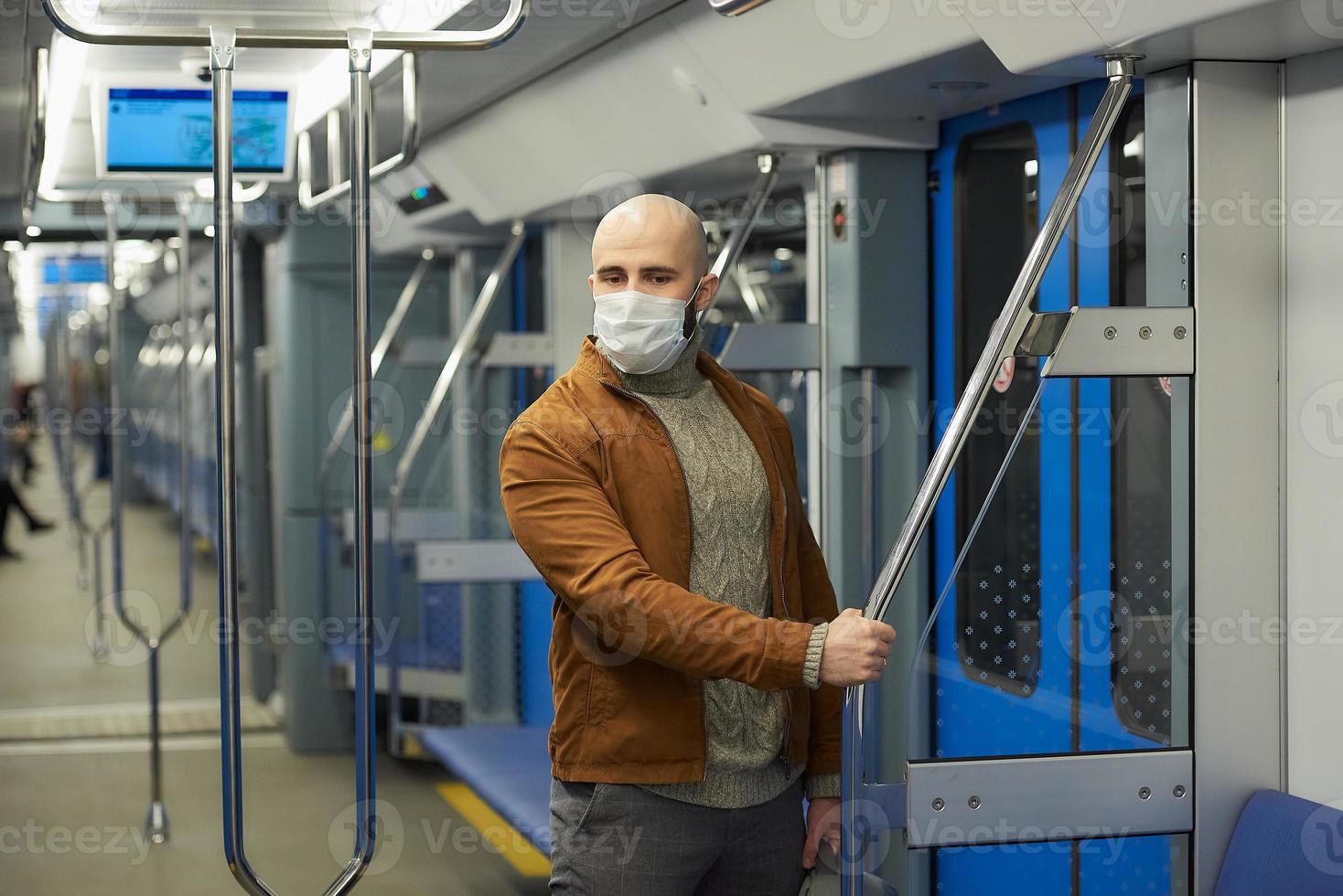 A bald man with a beard in a face mask is holding the handrail in a subway car photo