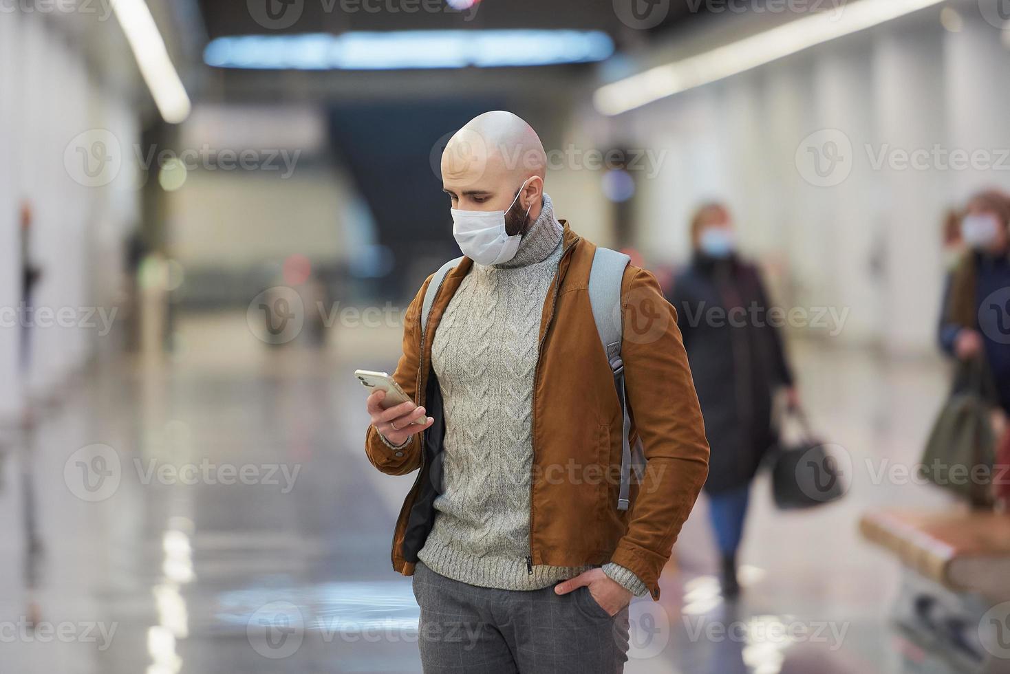 un hombre con una máscara facial está usando un teléfono inteligente mientras espera un tren subterráneo foto