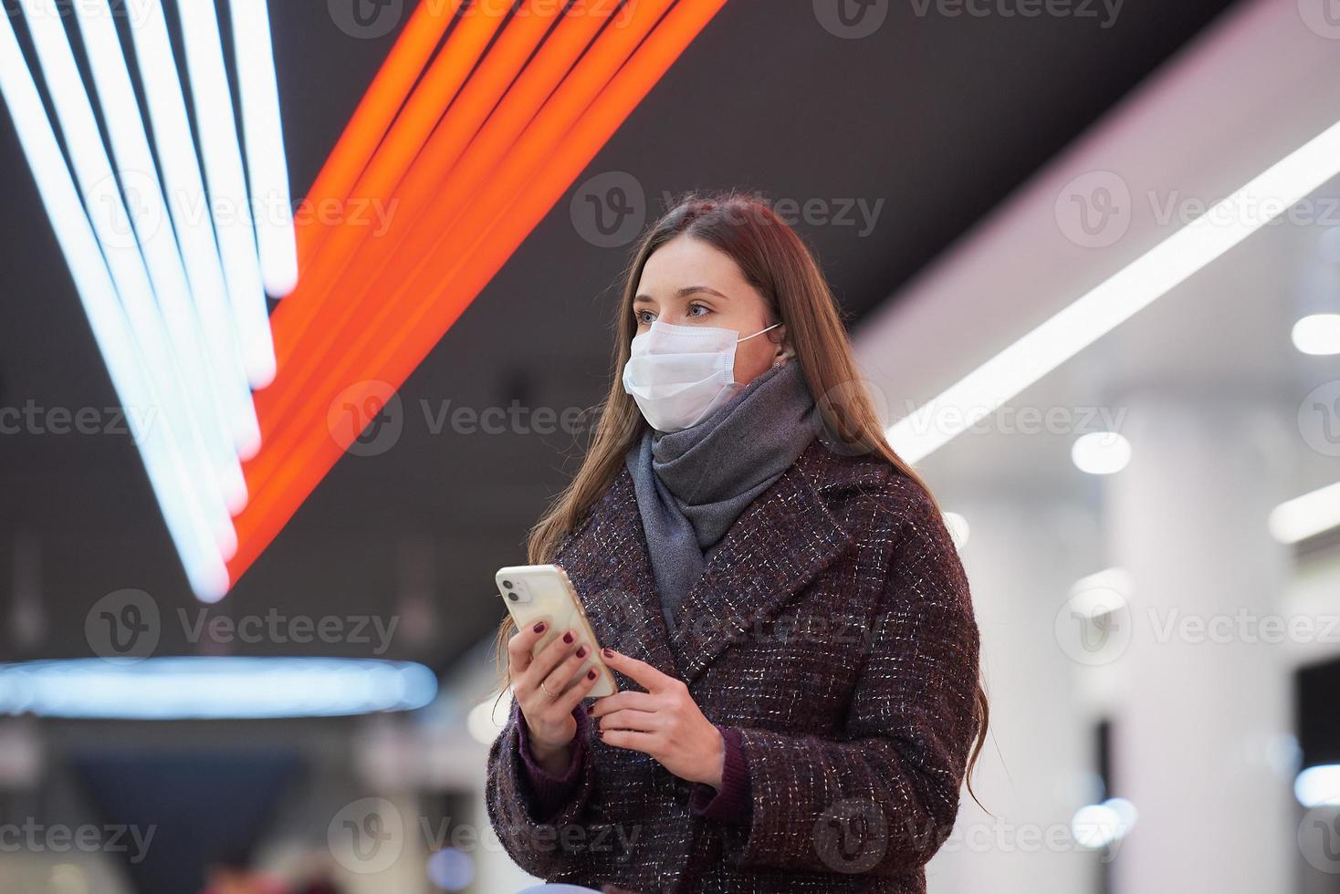 A woman in a medical face mask is waiting for a train and holding a smartphone photo