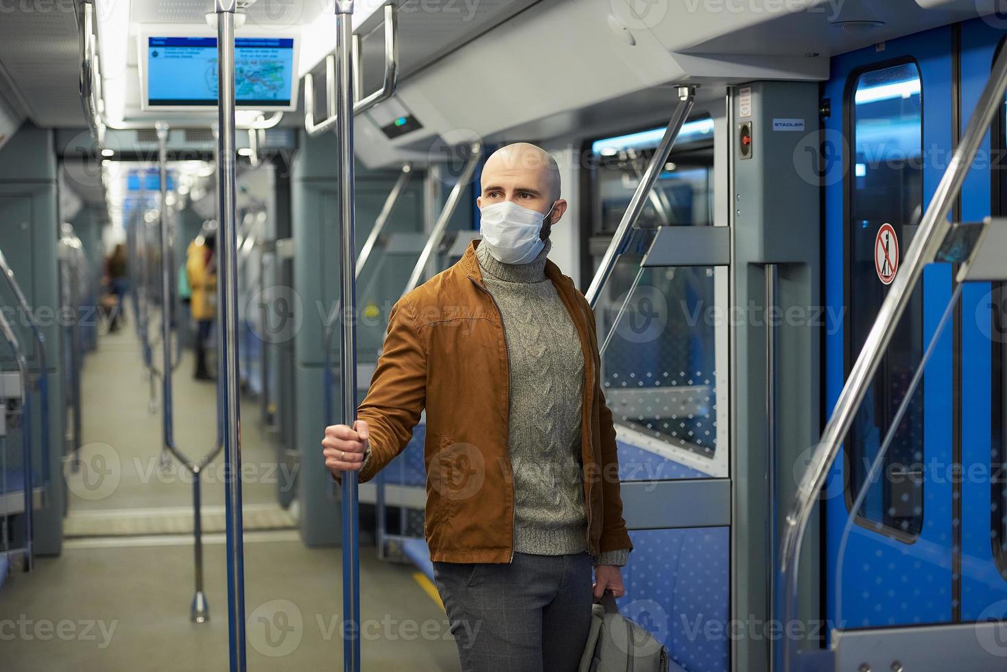 Un hombre calvo con barba en una mascarilla está sosteniendo el pasamanos en un vagón de metro foto