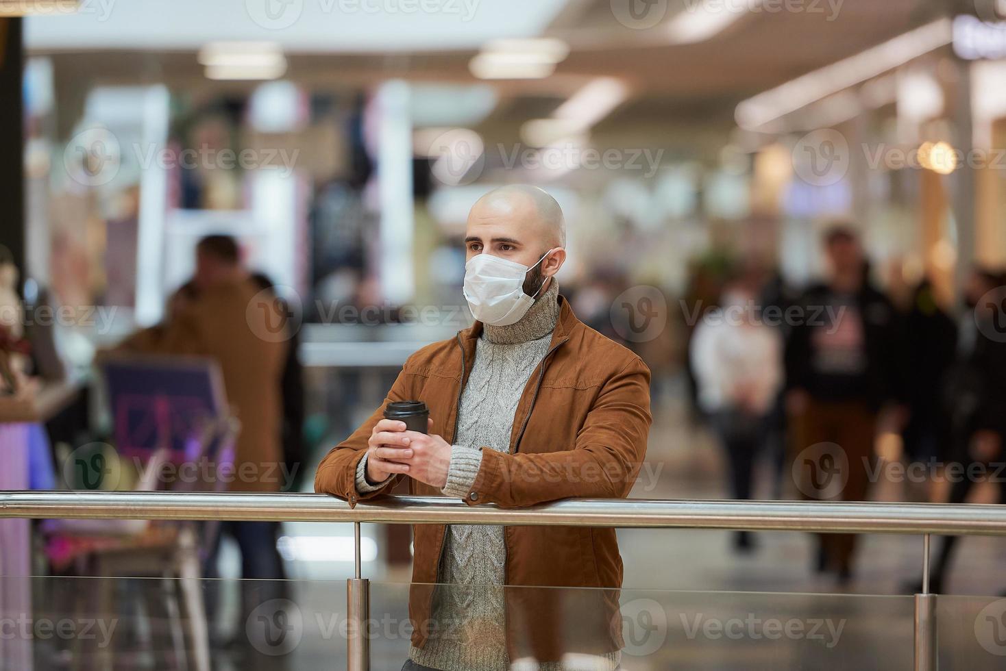 un hombre con una mascarilla está sosteniendo una taza de café en el centro comercial foto