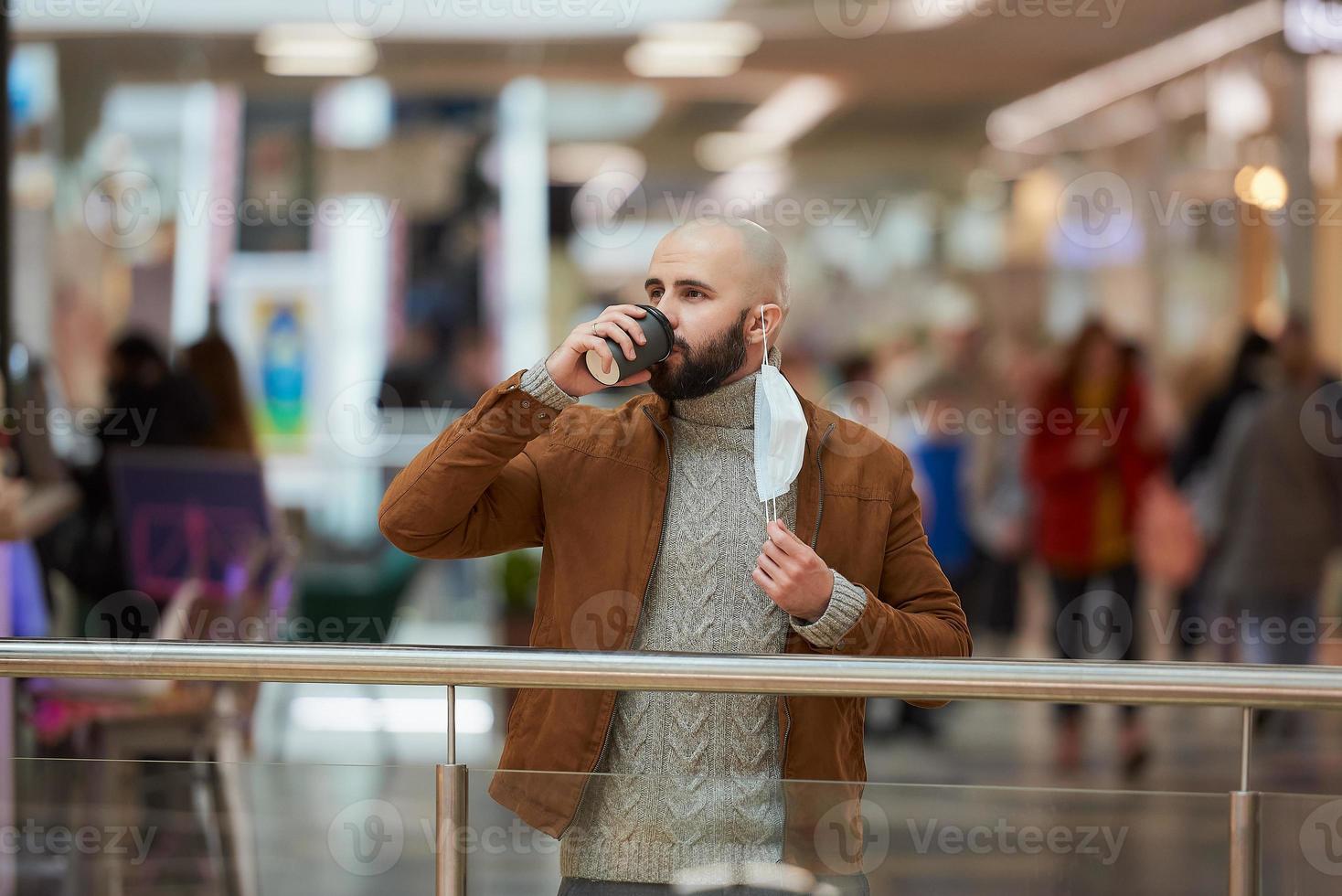 un hombre sostiene una máscara de despegue mientras toma café en el centro comercial foto