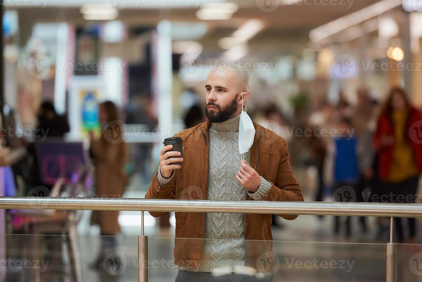 un hombre sostiene una máscara de despegue mientras toma café en el centro comercial foto