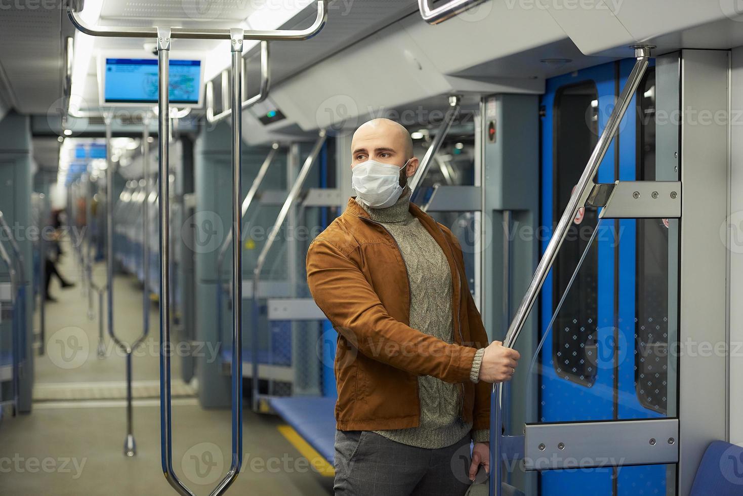 Un hombre calvo con barba en una mascarilla está sosteniendo el pasamanos en un vagón de metro foto