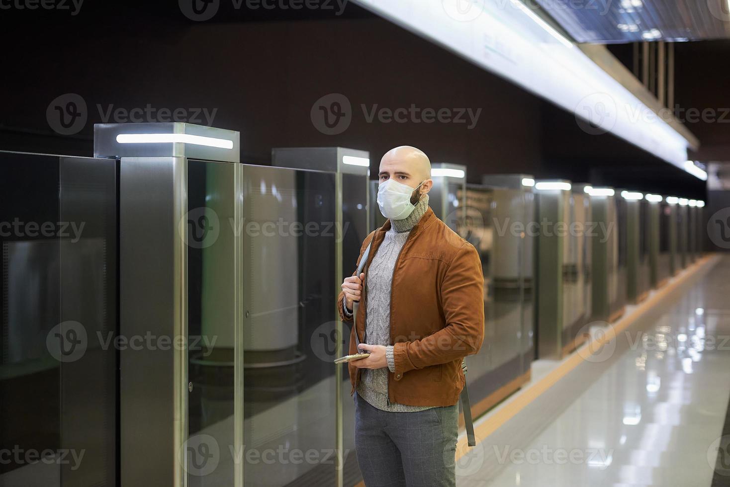 A man in a face mask is using a smartphone while waiting for a subway train photo