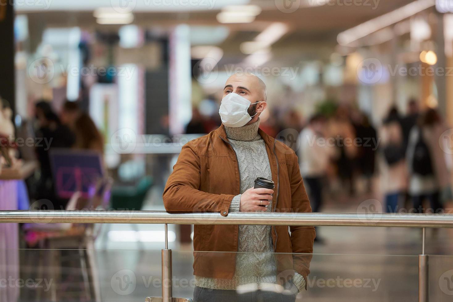 A man in a face mask is holding a cup of coffee in the shopping center photo