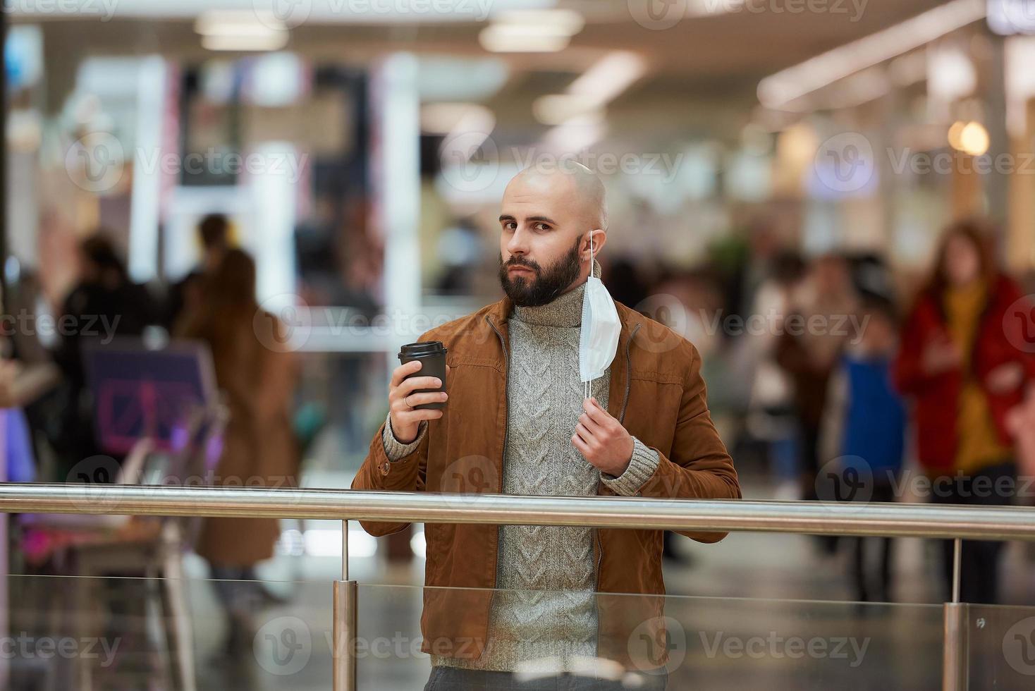 un hombre sostiene una máscara de despegue mientras toma café en el centro comercial foto