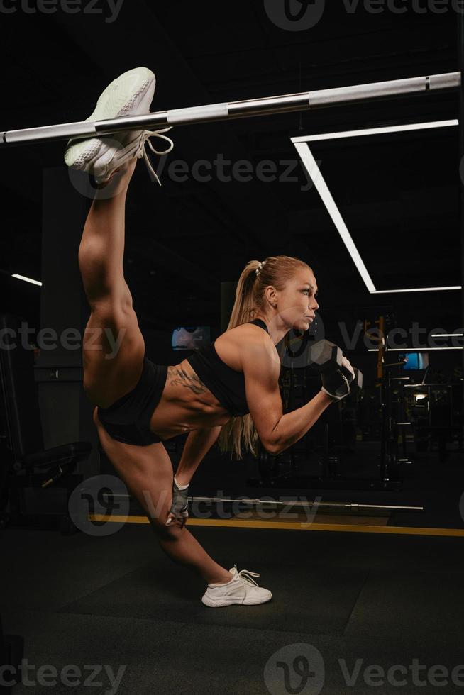 Una mujer con cabello rubio está haciendo un cordel durante los curls de bíceps con mancuernas en un gimnasio foto