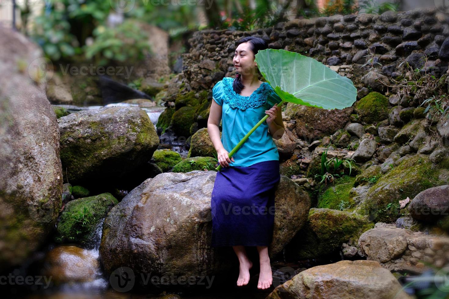 mujer sentada cerca del agua con una hoja gigante foto