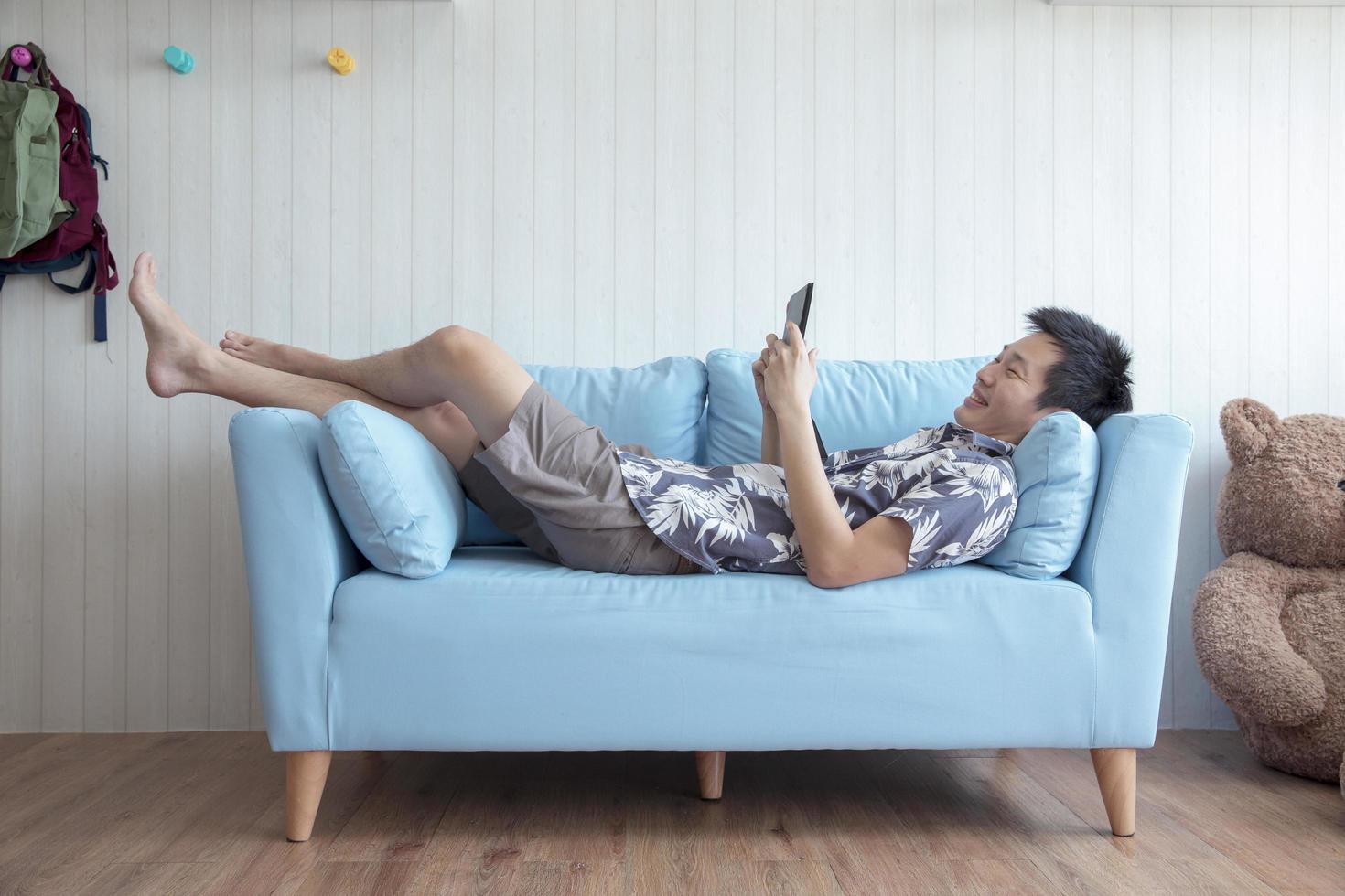 Happy young man lying on couch playing tablet at home in living room photo