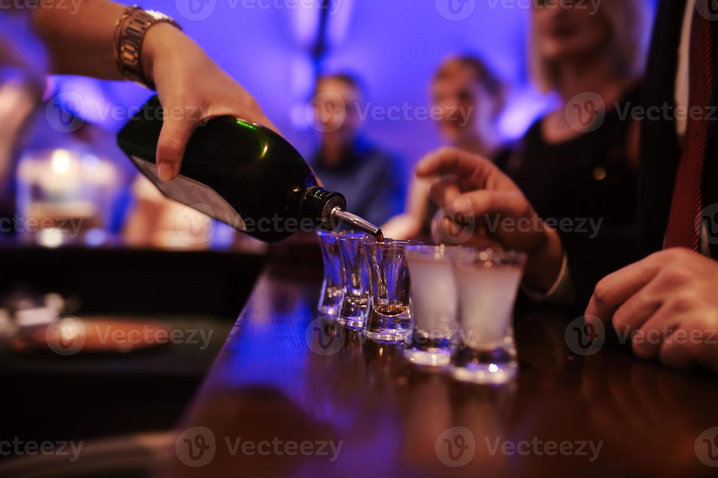 Camarero vertiendo bebidas alcohólicas fuertes en vasos pequeños en el bar, tragos en una discoteca o bar foto