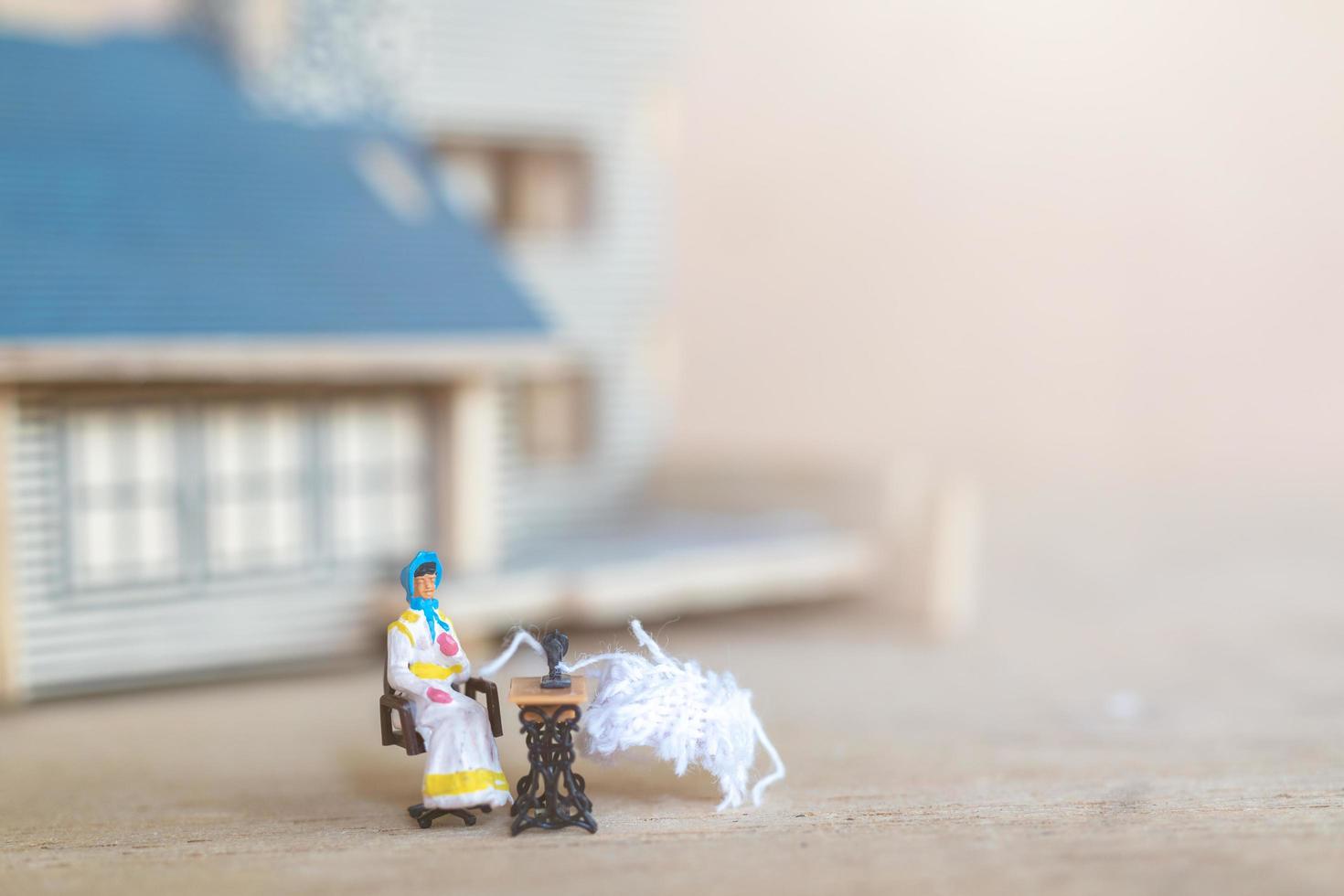 Miniature people, woman sewing on a sewing machine at her home. Woman seamstress working on a sewing-machine photo