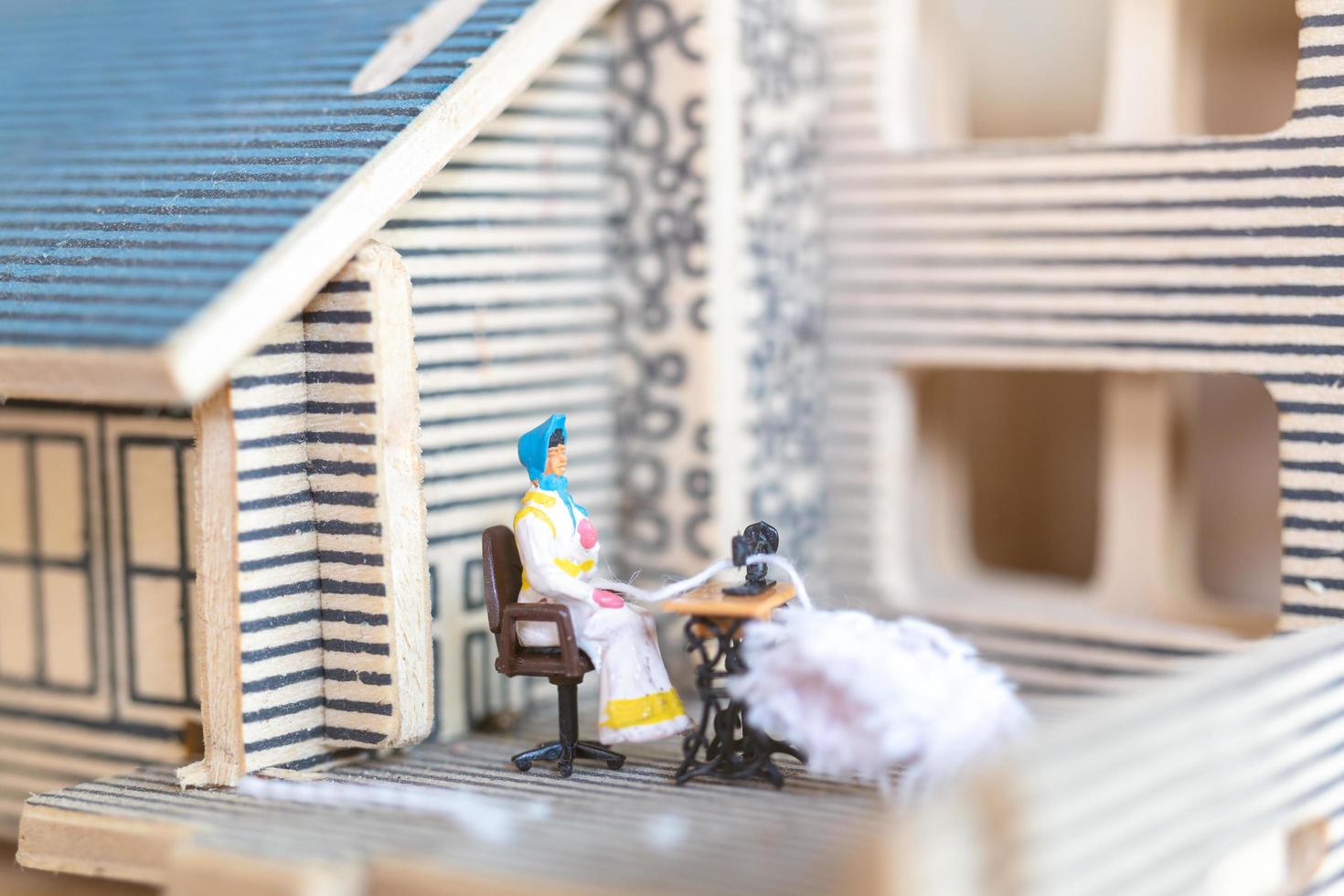 Miniature people, woman sewing on a sewing machine at her home. Woman seamstress working on a sewing-machine photo