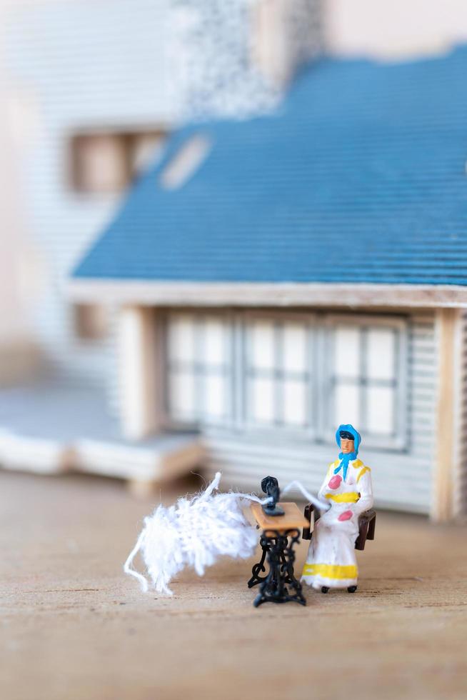 Miniature people, woman sewing on a sewing machine at her home. Woman seamstress working on a sewing-machine photo