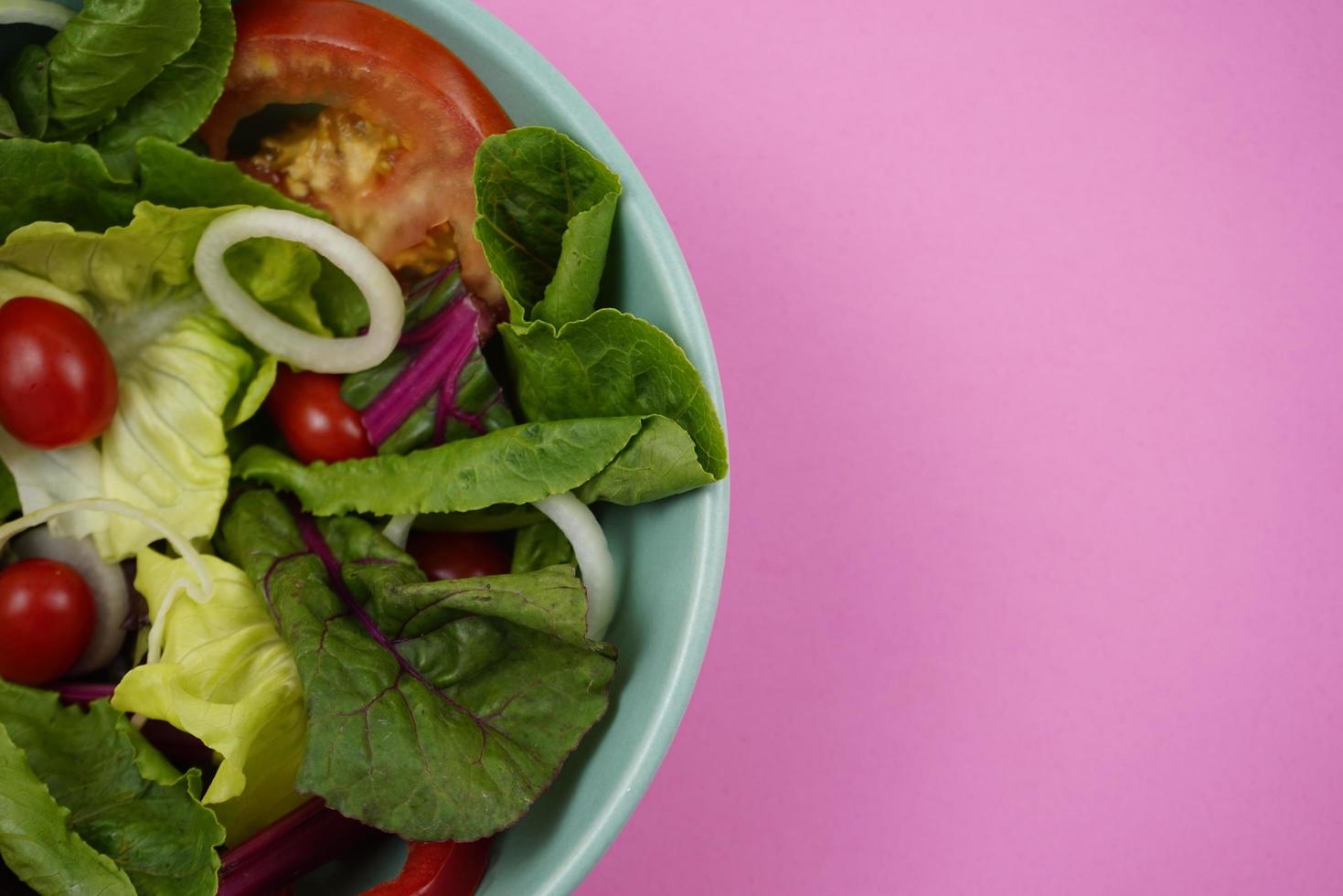 Ensalada de verduras, comida nutritiva dietética en un tazón verde sobre fondo rosa. foto