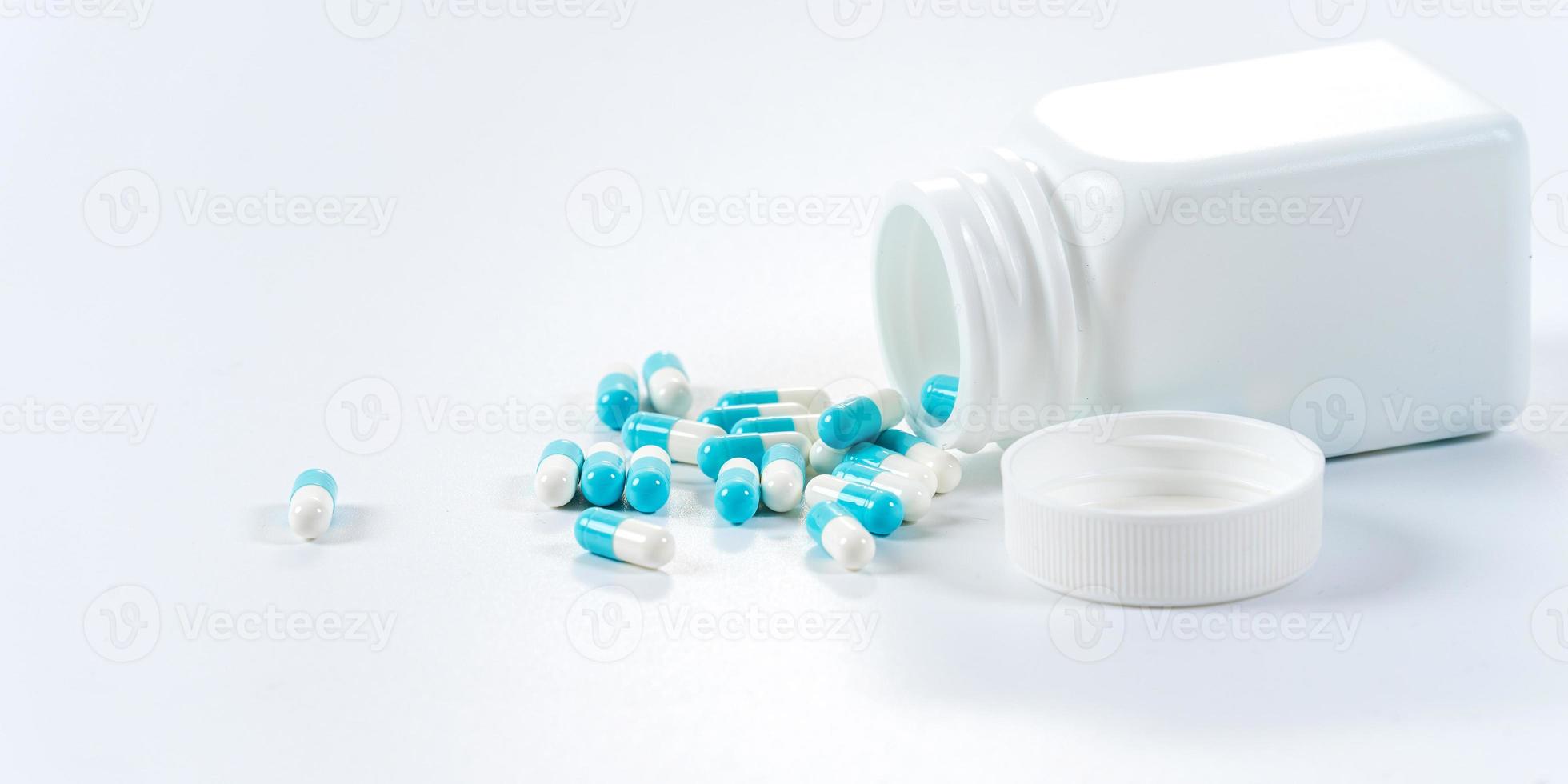 Blue and white capsules pills pouring from the bottle on white background photo