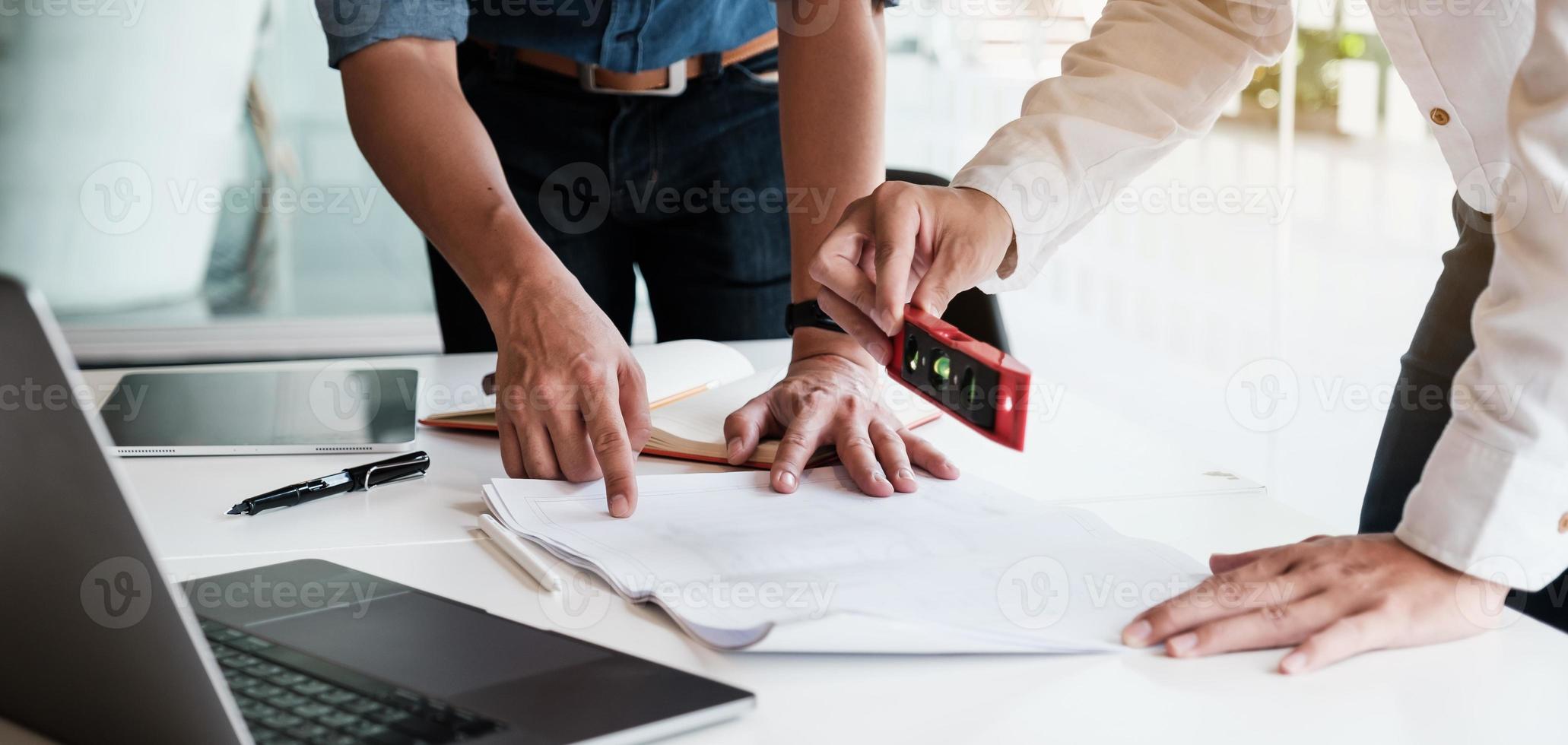 dos arquitectos masculinos que trabajan con una computadora portátil y planos para el plan arquitectónico, ingeniero esbozando un concepto de proyecto de construcción. foto