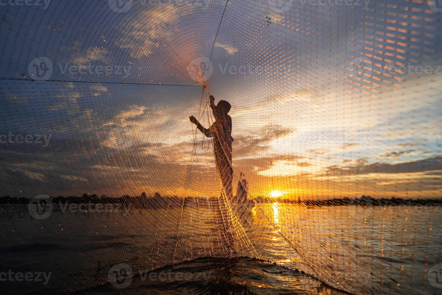 Silueta de pescador en barco de pesca con red en el lago al atardecer, Tailandia foto