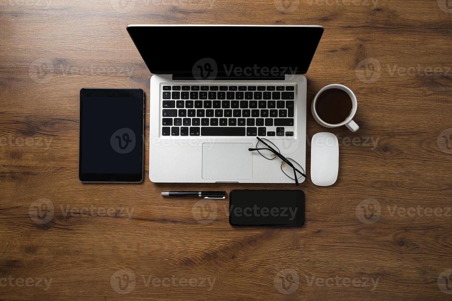 espacio de trabajo con computadora portátil, teléfono inteligente, tableta, taza de café, gafas y bolígrafo foto