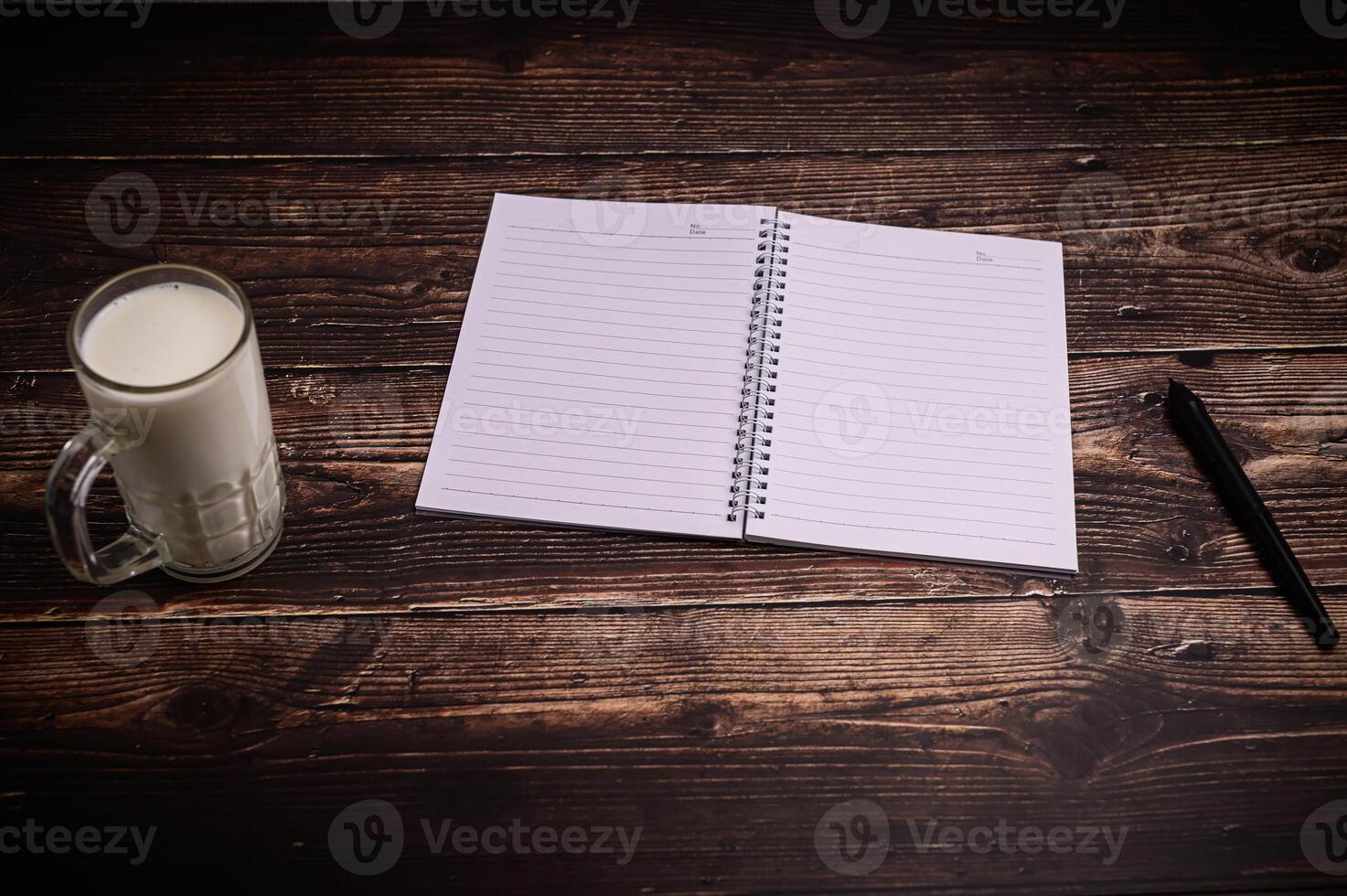 Notebook and glass of milk on wooden table photo