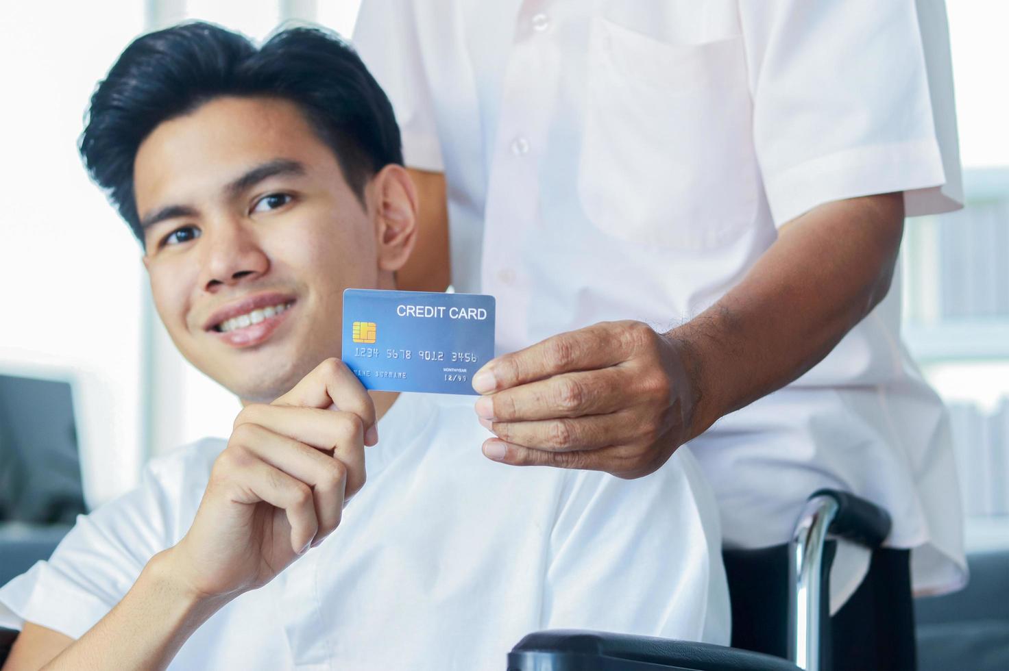 Male patient sitting in a wheelchair in a hospital holds a credit card photo