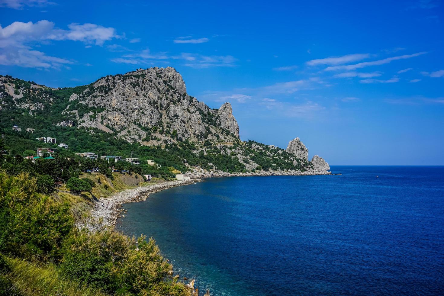 Rock covered with green vegetation hanging over the calm blue sea photo