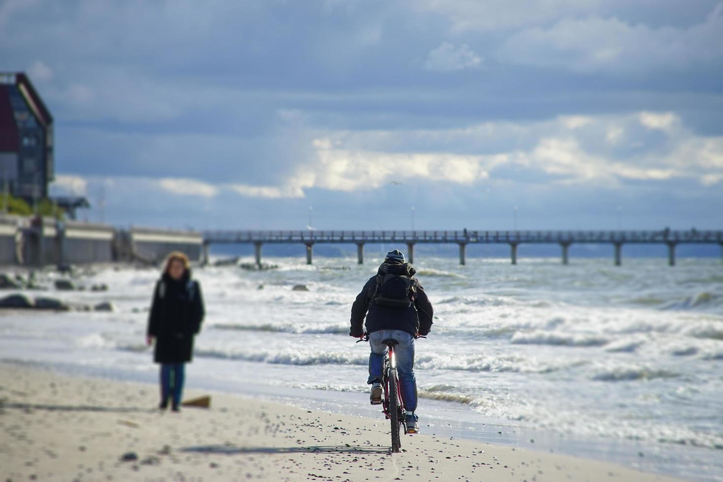 una anciana camina por la playa de arena hacia el ciclista. foto