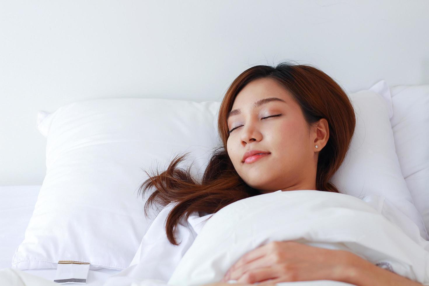 mujer asiática duerme en una cama blanca en unas vacaciones en casa. foto